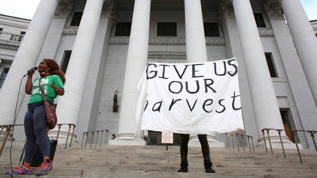 DonQuenick demands reparations and a protester raises a sign reading ?Give us our harvest in Denver, Colorado