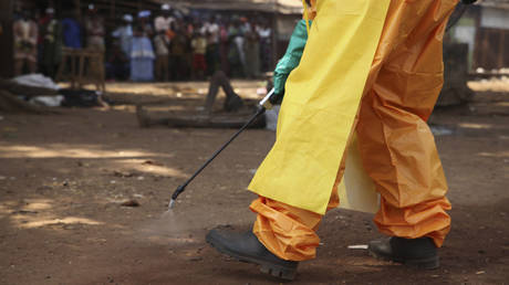 A member of the French Red Cross disinfects the area around a motionless person suspected of carrying the Ebola virus as a crowd gathers in Forecariah, Guinea, January 30, 2015.