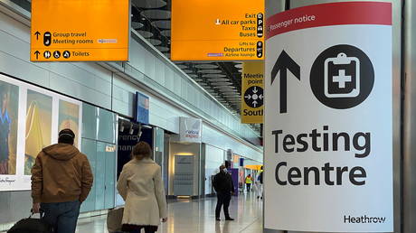 FILE PHOTO. Travellers pass a sign for a COVID-19 test centre at Heathrow Airport