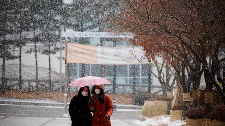 FILE PHOTO. Women wearing face masks walk under an umbrella as it snows in Seoul, South Korea.