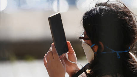 FILE PHOTO: A woman wearing a protective face mask holds a mobile phone in London, Britain, April 19, © Reuters / Steven Watt