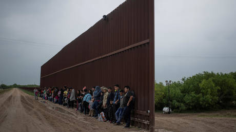 FILE PHOTO: Asylum-seeking migrants from Central America line-up along the border wall as they wait to surrender to the US border patrol, in Penitas, Texas, April 2, 2019.
