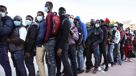 People who are seeking asylum in the United States wait in line to collect flyers explaining updated asylum policies outside the El Chaparral border crossing on February 19, 2021 in Tijuana, Mexico