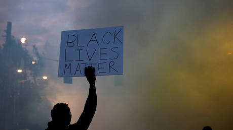 FILE PHOTO: A person holds a "Black Lives Matter" sign as a heavy cloud of tear gas and smoke rises after being deployed by Seattle police as protesters rally against police brutality and the death in Minneapolis police custody of George Floyd.