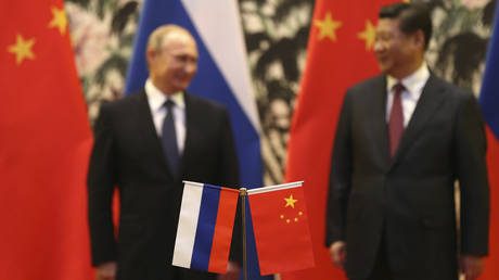 Russian and Chinese national flags are seen on the table with Russian President Vladimir Putin (L) and his Chinese counterpart Xi Jinping stand in the background during a signing ceremony at the Diaoyutai State Guesthouse in Beijing, November 9, 2014. © Reuters / How Hwee Yong