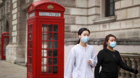 Women wearing face masks walk on a street in London, February 22, 2021
