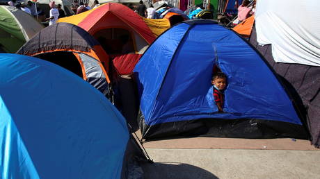 A child looks out from a tent next to other migrants from Central America who are camping outside the El Chaparral border crossing, hoping to cross and request asylum in the U.S. , in Tijuana, Mexico February 27, 2021. © REUTERS/Jorge Duenes