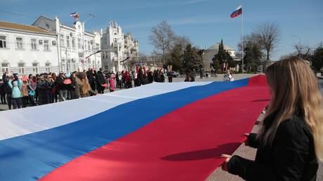 Participants of a flash mob dedicated to the sixth anniversary of the reunification of Crimea with Russia unfurl the Russian flag in the center of Yevpatoria.© RIA