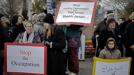 FILE PHOTO. Peace demonstrators raise signs during a protest near the house of a Palestinian family, which an Israeli court had ordered to be evicted while declaring Israeli settlers to be the legal owners, in the East Jerusalem neighbourhood of Sheikh Jarrah. © AFP / THOMAS COEX