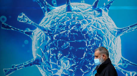 A man wearing a protective face mask walks past an illustration of a virus outside a regional science centre