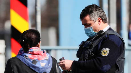 A police officer checks a commuter arriving from Poland, at the German-Polish border crossing in Frankfurt, Germany, March 22, 2021.