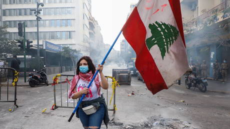 A demonstrator carries a national flag along a blocked road, during a protest against the fall in Lebanese pound currency and mounting economic hardships, near the Central Bank building, in Beirut, Lebanon (FILE PHOTO) © REUTERS/Mohamed Azakir