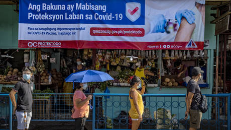 A streamer showing information on COVID-19 vaccines is seen as Filipinos queue outside a wet market to stock up on food a day before a strict lockdown is reimposed in Manila and nearby provinces on March 28, 2021 in Quezon city, Metro Manila, Philippines.