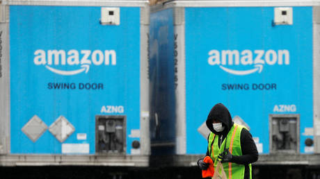 FILE PHOTO: A worker walks by trucks parked at an Amazon facility in Long Island, New York.