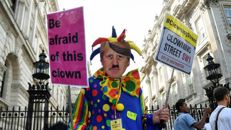 FILE PHOTO: An anti-Brexit protester wearing a clown costume and a defaced mask depicting British Prime Minister Boris Johnson holds placards in Westminster in London, UK, August 29, 2019 © Reuters / Toby Melville