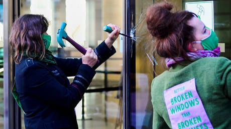 An activist from the Extinction Rebellion, a global environmental movement, damages a window during a direct action at Barclays offices in Canary Wharf, London, Britain, April 7, 2021 © REUTERS / Toby Melville