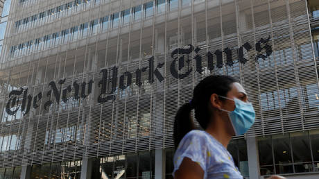 A woman wearing a protective face mask walks by the New York Times building in Manhattan