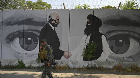 A security personnel walks past a wall mural with images of US Special Representative for Afghanistan Reconciliation Zalmay Khalilzad (L) and Taliban co-founder Mullah Abdul Ghani Baradar, in Kabul on July 31, 2020.