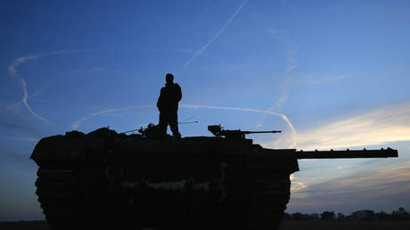 An Israeli soldier atop a tank looks at air force fighter jets circling overhead