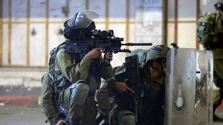 An Israeli soldier aims his weapon while others take cover behind their shields during a Palestinian protest amid a flare-up of Israeli-Palestinian violence, in Hebron in the Israeli-occupied West Bank, May 11, 2021 © Reuters / Mussa Qawasma
