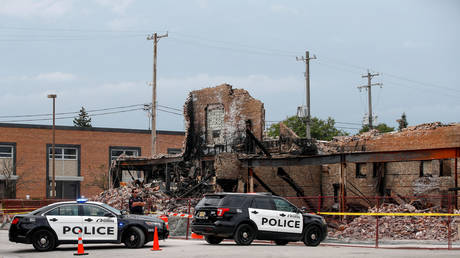 Kenosha, Wisconsin police outside a building burned down in August 2020; The Intercept accused eight reporters of 'smearing' Black Lives Matter with their riot footage.