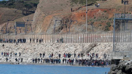Migrants run towards the fence separating Morocco from Spain, after thousands of migrants swam across the border, in Ceuta, Spain, May 19, 2021. © REUTERS/Jon Nazca