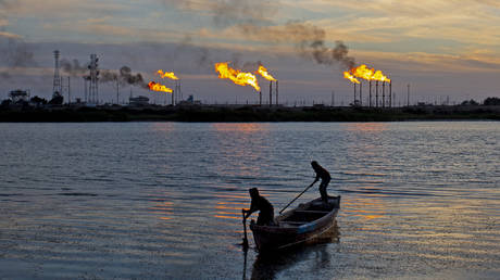 Iraqi fishermen row their boat across flare stacks burning at the Nahr Bin Omar field, north of the southern Iraqi port of Basra