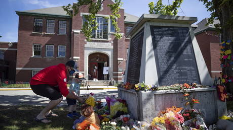 Jaret Hamm and his son John Hamm, 2, place flowers beside a monument outside the former Kamloops Indian Residential School in Kamloops, British Columbia, on Monday, May 31, 2021. © Darryl Dyck/The Canadian Press via AP