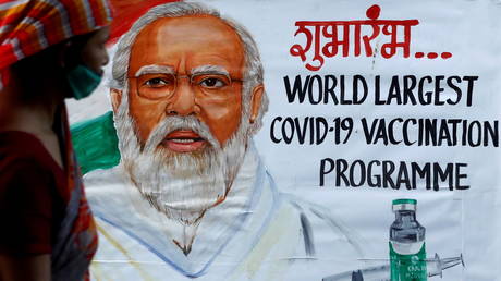 A woman walks past a painting of Indian Prime Minister Narendra Modi a day before the inauguration of the COVID-19 vaccination drive, on a street in Mumbai, India, (FILE PHOTO) © REUTERS/Francis Mascarenhas