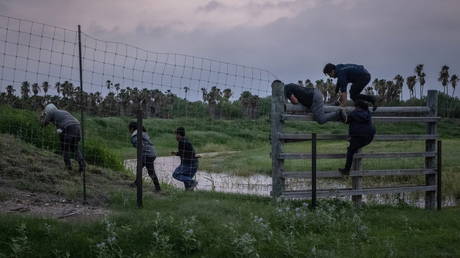 Migrants from Central America, pursued by US Border Patrol, jump a fence into private property in La Joya, Texas, after crossing the Rio Grande river into the US from Mexico, May 18, 2021.