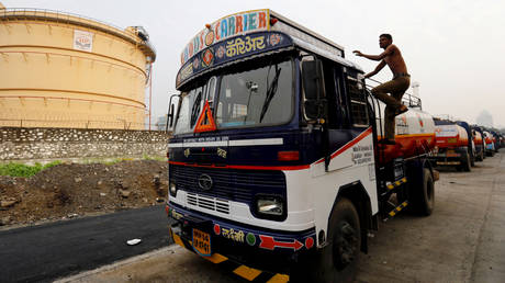 A man climbs an an oil tanker parked outside a fuel depot in Mumbai, India