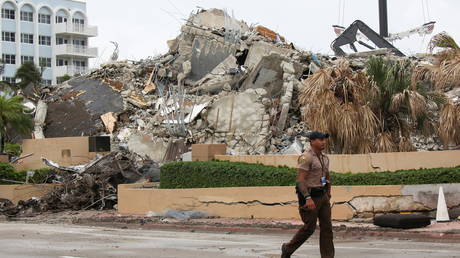 A police officer walks in front of debris at the Champlain Towers South complex following a catastrophic collapse, in Surfside, Florida, July 6, 2021.