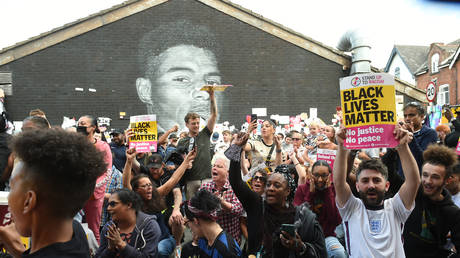 Demonstrators hold up banners in front of the Marcus Rashford mural after it was defaced following the Euro 2020 Final between Italy and England, in Manchester, Britain, July 13, 2021.