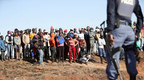 A police officer stands guard in front of protesters as the country deploys the army to quell unrest linked to the jailing of former South African President Jacob Zuma, in Vosloorus, South Africa, July 14, 2021. © REUTERS/Siphiwe Sibeko