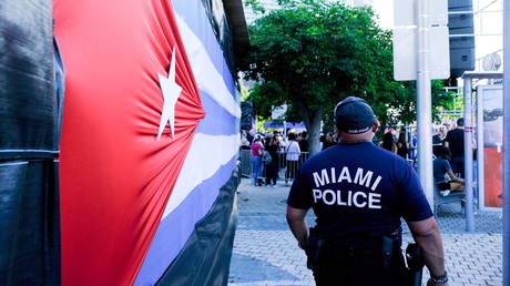 A Miami police officer stands next to a Cuban flag as emigres gather at the Freedom Tower in reaction to reports of protests in Cuba against its deteriorating economy, in Miami, Florida, U.S. July 17, 2021. © Reuters / Maria Alejandra Cardona