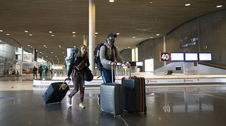 Travelers wearing face masks push their suitcases in hallways at Roissy Charles De Gaulle airport during the Coronavirus (COVID)19) pandemic on May 14, 2020 in Paris, France. © Aurelien Meunier/Getty Images