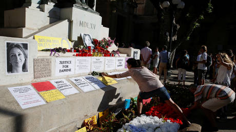 People place flowers on a makeshift memorial during a protest and vigil marking twenty-one months since the assassination of anti-corruption journalist Daphne Caruana Galizia. © REUTERS/Darrin Zammit Lupi