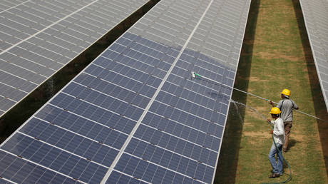 Workers clean photovoltaic panels inside a solar power plant in Gujarat, India
