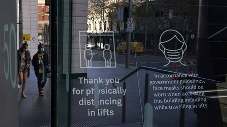 People wearing protective face masks walk past signs in the lobby of a City Centre building outlining public health guidelines during a lockdown to curb the spread of the coronavirus disease (COVID-19) outbreak in Sydney, Australia, July 21, 2021. © REUTERS/Loren Elliott