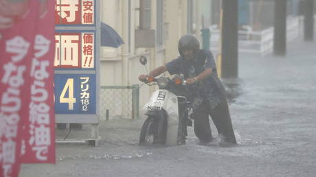 A man pushes a motorbike in a road flooded by heavy rain in Kurume, Fukuoka prefecture, western Japan, August 14, 202 © REUTERS /Kyodo