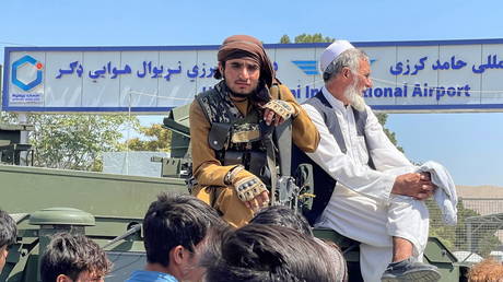 A member of Taliban forces (L) sits on a an armoured vehicle outside Hamid Karzai International Airport in Kabul, Afghanistan August 16, 2021 © REUTERS/Stringer