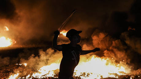 A Palestinian protester swings a slingshot near burning tyres during a demonstration along the border between the Gaza Strip and Israel. © AFP / Mahmud Hams