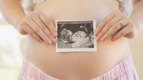 Woman holding sonogram over pregnant belly - stock photo © Getty images.