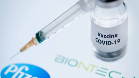 This illustration picture taken on November 23, 2020 shows a bottle reading "Vaccine Covid-19" and a syringe next to the Pfizer and Biontech logo. © AFP / Joel Saget
