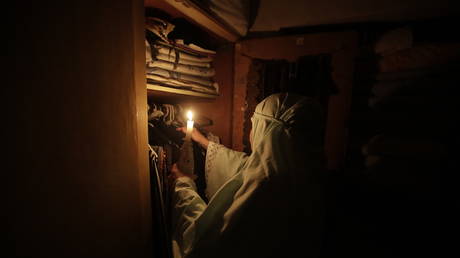 A Lebanese woman uses light from a candle to put away clothes in the capital Beirut on July 10, 2021, amid severe power outages in the crisis-hit country. © AFP / Anwar Amro