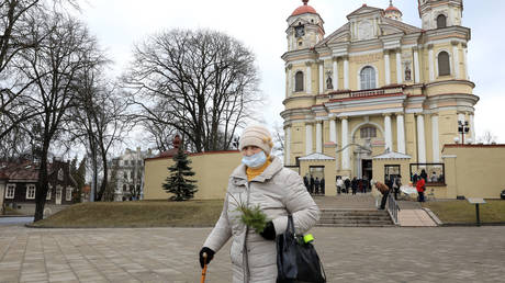 A woman wearing a face mask holds juniper twigs after a Palm Sunday mass outside the church of St Peter and St Paul in Vilnius, Lithuania, on March 28, 2021, amid the novel coronavirus / COVID-19 pandemic. © AFP / Petras Malukas