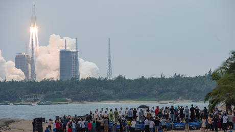 People watch from a beach as the Long March-5B Y2 rocket, carrying the core module of China's space station Tianhe, takes off - April 29, 2021