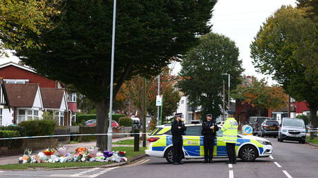 Police officers staff a cordon next to floral tributes left near the scene of the fatal stabbing of British lawmaker David Amess close to Belfairs Methodist Church in Leigh-on-Sea, a district of Southend-on-Sea, in southeast England on October 17, 2021. © AFP / Adrian DENNIS