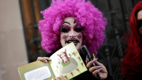 A participant dressed in drag shows a book during a Drag Queen Story Hour event