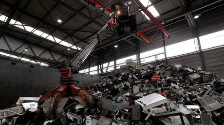 A worker in a crane uses a grappler to grab electronic scrap